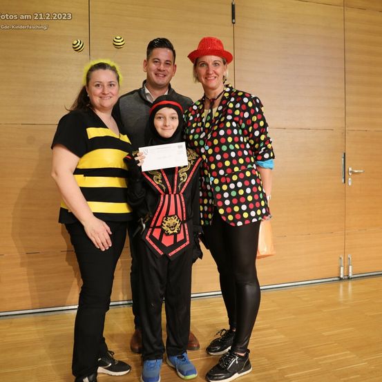 Vier Personen in thematischen Kostümen posieren für ein Foto, eine hält ein Zertifikat. Die Frau links trägt ein Bienenkostüm. Der Mann in der Mitte lächelt. Eine Frau rechts trägt ein Punktehemd. Das Bild ist vom 21.2.2023.