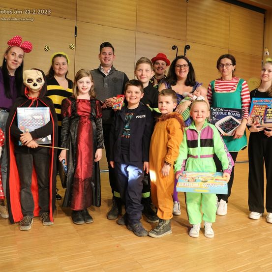 Eine Gruppe von Erwachsenen und Kindern in Kostümen posiert für ein Foto mit Büchern und Spielzeug, datiert auf den 21.2.2023.