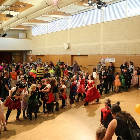 Eine große Gruppe von Kindern in Kostümen tanzt auf einem Holzboden. Das Datum 21.2.2023 ist in der oberen linken Ecke sichtbar.