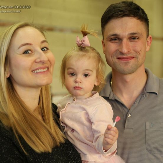 Eine dreiköpfige Familie lächelt für ein Foto. Eine Frau und ein Mann mit einem Mädchen in der Mitte. Das Mädchen hält einen Lutscher. Das Foto wurde am 21. Februar 2023 aufgenommen.