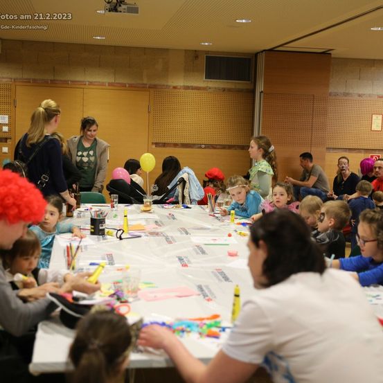 Gruppe von Kindern und Erwachsenen um einen langen Tisch versammelt, die sich mit Luftballons, Bastelmaterial und Markern am 21.2.2023 beschäftigen.
