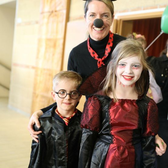 Eine Frau in einer Katzenkostüm posiert mit zwei Kindern, eines gekleidet als Hexe und das andere als Junge in einer Schuluniform.