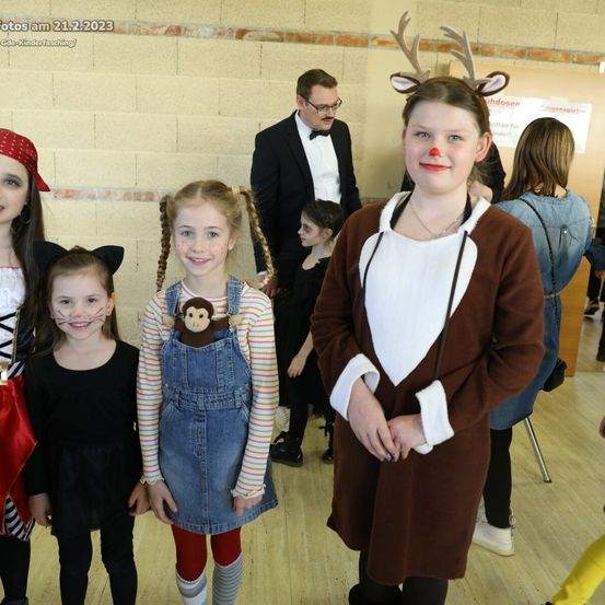 Eine Gruppe von Kindern in Kostümen posiert für ein Foto am 21. Februar 2023. Sie befinden sich in einem Raum mit Ziegelwand und Holzboden.