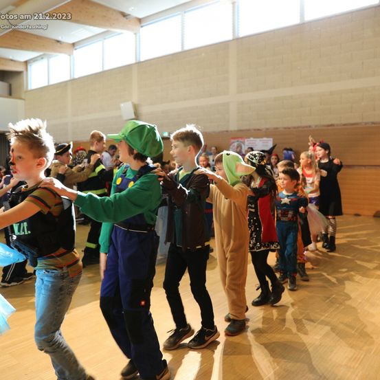 Kinder in Kostümen tanzen am 21. Februar 2023 in einer Turnhalle mit Holzboden und großen Fenstern.