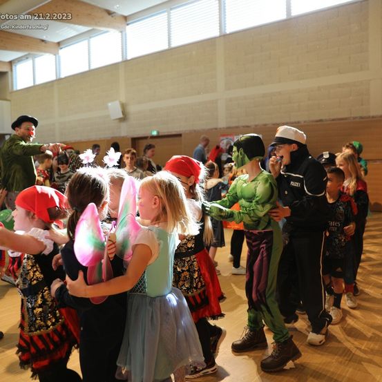 Eine Gruppe von Kindern in Kostümen tanzt am 21. Februar 2023 in einer Halle. Unter ihnen ein Kind als Hulk verkleidet und ein Polizist.