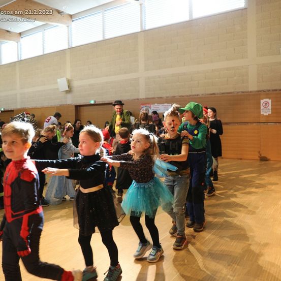 Kinder in Kostümen tanzen am 21. Februar 2023 in einer großen Halle. Einige tragen Superheldenkostüme, während andere in Feenkostümen oder als magische Kreaturen gekleidet sind.