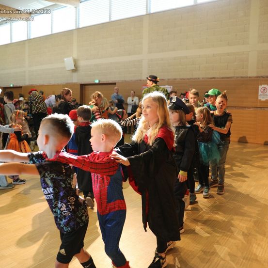 Eine Gruppe von Kindern in Kostümen tanzt auf einem Holzboden, umgeben von anderen Kindern und Erwachsenen. Einige sind in Halloween-Kleidung. Ein Wasserzeichen zeigt an, dass das Foto am 21. Februar 2023 aufgenommen wurde.