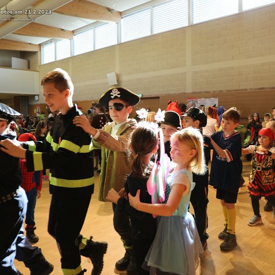 Kinder in verschiedenen Kostümen, darunter Piraten, Feen und Superhelden, tanzen in einer Schulturnhalle. Das Bild wurde am 21. Februar 2023 aufgenommen.