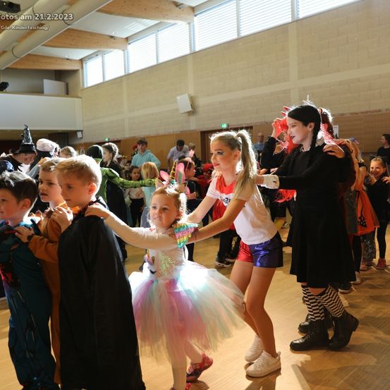 Kinder in Kostümen tanzen bei einer Hallenveranstaltung am 21.2.2023. Ein Mädchen in einem Tutu hält die Hand eines Jungen in einem schwarzen Umhang.