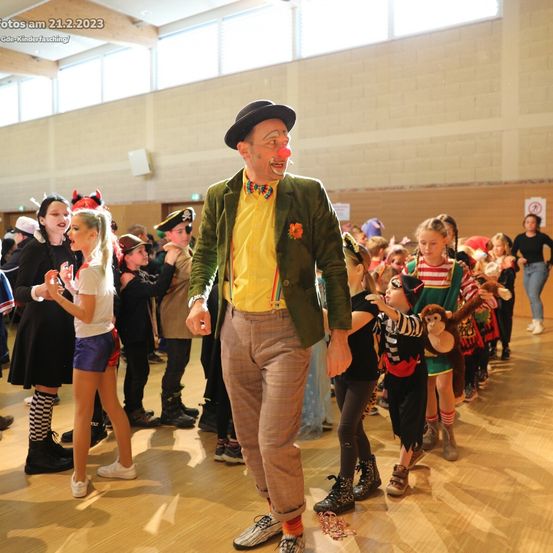 Ein Clown geht vor einer Reihe von Kindern in Kostümen, drinnen, am 21. Februar 2023.
