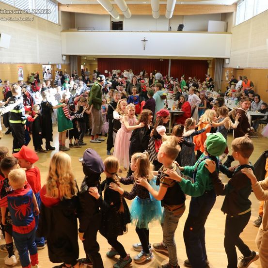 Eine große Gruppe von Kindern in Kostümen tanzt am 21. Februar 2023 in einem Saal. Einige sind in Superheldenkostümen, während andere verschiedene thematische Kostüme tragen.
