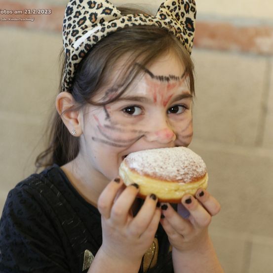 Ein Mädchen, das in einem Leoparden-Kopfband und mit Gesichtsbemalung verkleidet ist, isst am 21. Februar 2023 einen mit Puderzucker bestreuten Donut.