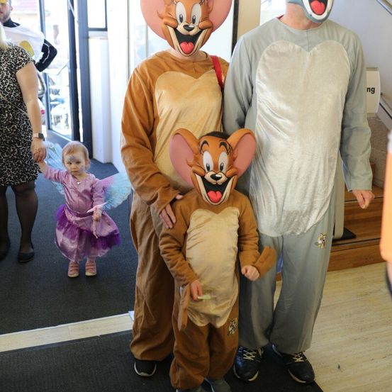 Eine Familie aus drei Personen, gekleidet in Tom-und-Jerry-Kostümen, steht zusammen mit einem kleinen Mädchen in einem Feenkostüm in einem Flur.
