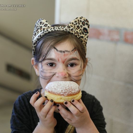 Ein junges Mädchen mit Gesichtsbemalung hält einen mit Puderzucker bestreuten Donut, aufgenommen am 21. Februar 2023.