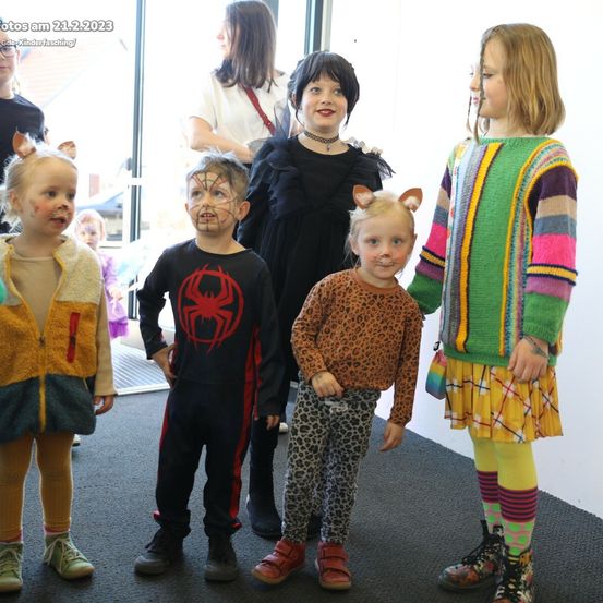 Eine Gruppe von Kindern in verschiedenen Kostümen, darunter einer als Spider-Man, steht vor einer Glastür, mit Erwachsenen dahinter. Das Foto wurde am 21. Februar 2023 aufgenommen.