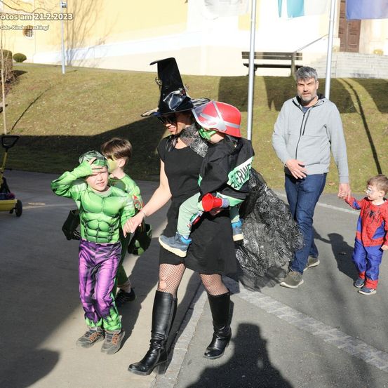 Eine Familie läuft auf einer Straße mit Kindern in Kostümen. Eine Frau trägt einen Hexenhut und hält ein Kind in einer Feuerwehrausrüstung. Dahinter ein Mann und ein Kind in einem Spider-Man-Kostüm. Das Foto ist vom 21.2.2023.