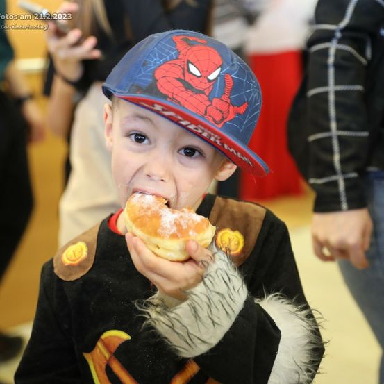 Ein junger Junge in einer Spider-Man-Kappe isst einen Donut. Gedatet am 21.2.2023, er trägt ein Superheldenkostüm.