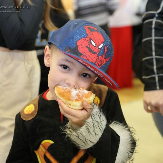 Ein kleiner Junge isst einen Donut und trägt eine Spiderman-Kappe. Er hat ein Superheldenkostüm an. Das Foto wurde am 21. Februar 2023 aufgenommen.
