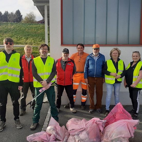 Eine Gruppe von Menschen in Sicherheitswesten und Turnschuhen steht neben einem Gebäude mit Säcken voller Müll auf dem Boden.