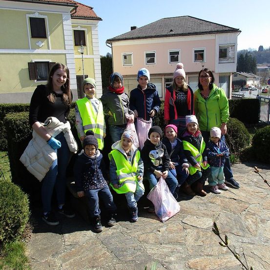 Eine Gruppe von Kindern und Erwachsenen posiert für ein Foto vor einem Haus. Sie tragen Sicherheitswesten und halten Tüten.