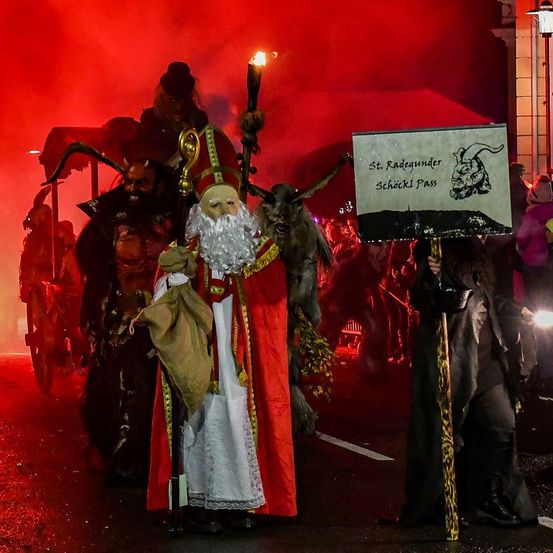 Ein nächtlicher Umzug mit Menschen in Kostümen, einer als St. Nikolaus verkleidet mit einer Fackel, hält ein Schild mit St. Radegund.