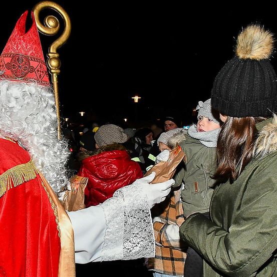Der Weihnachtsmann in einem roten Kostüm verteilt nachts in der Stadt Tüten mit Süßigkeiten an Kinder.