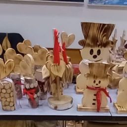 Ein Tisch mit Holzschmuck, darunter Schneemänner, Kerzen und herzförmige Dekorationen, ordentlich angeordnet. Hinter dem Tisch eine Wand mit gerahmten Bildern.