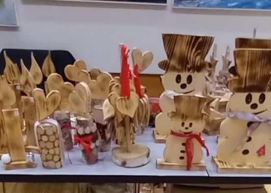 Ein Tisch mit Holzschmuck, darunter Schneemänner, Kerzen und herzförmige Dekorationen, ordentlich angeordnet. Hinter dem Tisch eine Wand mit gerahmten Bildern.