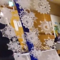 Ein weißes schneeklöckchenartiges Design ist prominent mit einem blauen Rand dargestellt. Im Hintergrund sitzt ein Mann an einem Schreibtisch.