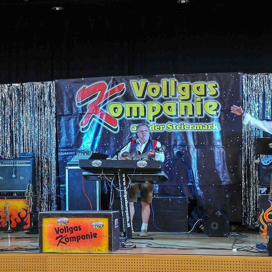 Ein Mann spielt Gitarre auf der Bühne mit einem Keyboard vor ihm. Hinter ihm ist ein Banner mit den Worten "Vollgas Kompanie".