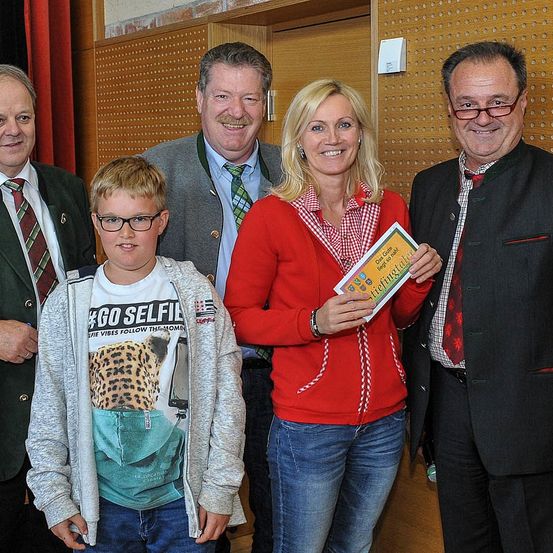 Eine Gruppe von fünf Personen posiert für ein Foto; eine Frau hält ein Buch und ein Junge trägt eine Brille. Hinter ihnen hat eine Wand ein Muster aus Löchern.