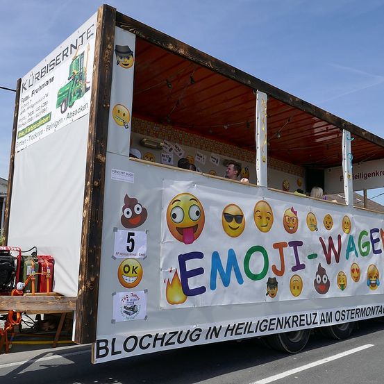 Ein Lastwagen mit einem Emoji-Wagen-Banner an der Seite ist auf der Straße geparkt. Im Inneren steht eine Person in der Nähe des Fensters. Der Lastwagen hat ein offenes Dach und ist mit Emojis dekoriert.