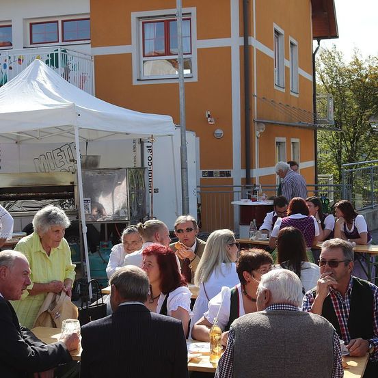 Eine Gruppe von Menschen sitzt unter einem Zelt in einem Außenbereich. Sie scheinen ihr Essen und Getränke zu genießen. Ein Foodtruck ist in der Nähe geparkt.