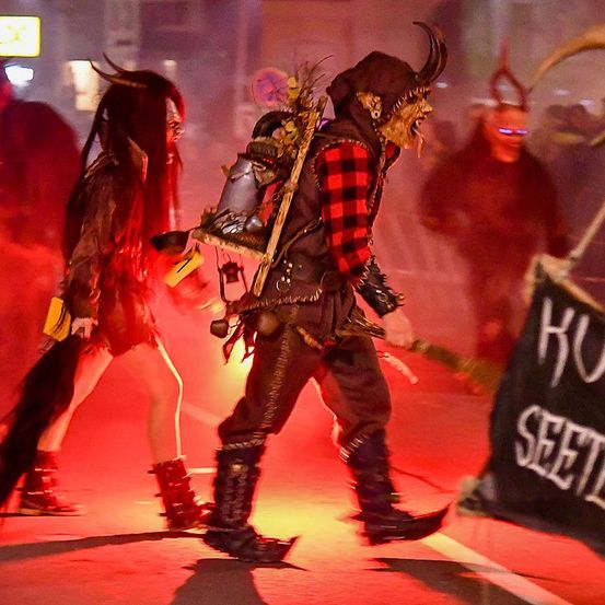 Zwei kostümierte Personen gehen bei einer Veranstaltung zusammen auf einer Straße, eine trägt einen gehörnten Helm und die andere eine Laterne und ein Schwert.