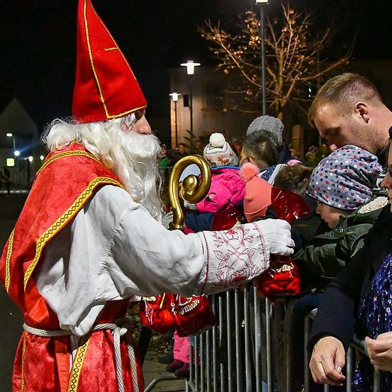 Ein Mann in einer Weihnachtsmann-Verkleidung verteilt nachts Geschenke an Kinder durch einen Zaun.