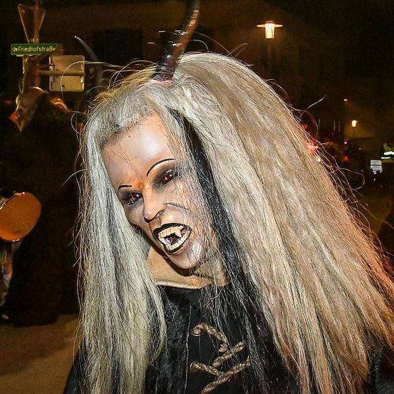 Eine Person mit einer langen blonden Perücke und einem Halloween-Kostüm steht draußen bei Nacht, wobei ein Straßenschild und Straßenlaternen im Hintergrund zu sehen sind.