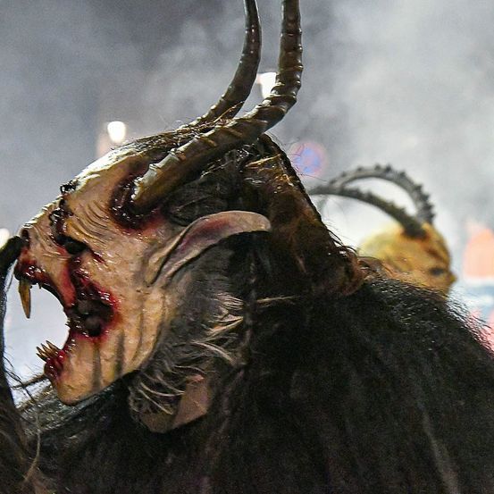 Eine Person mit einer grotesken Hörnermaske brüllt mit Blut um den Mund, möglicherweise für eine Halloween-Veranstaltung.