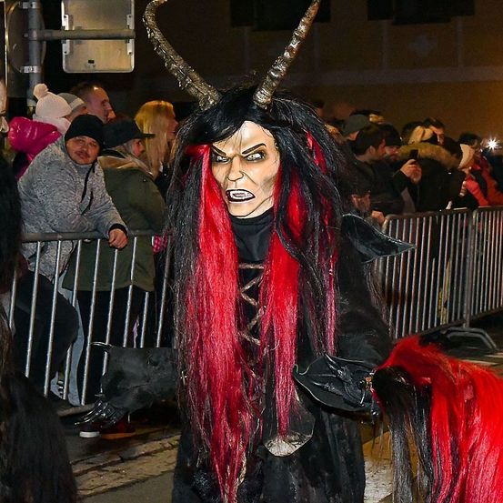 Eine Person in einem Dämonenkostüm mit Hörnern steht vor einer Menge, möglicherweise bei einer Halloween-Veranstaltung.