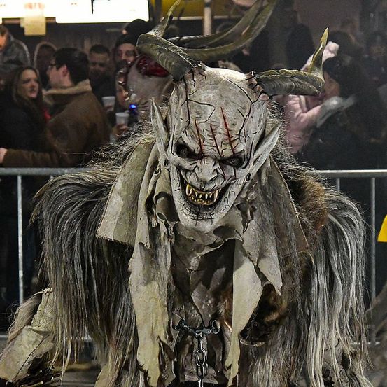 Eine Person in einem gruseligen Hörnerkostüm steht vor einer Menge bei einer Veranstaltung, möglicherweise einer Halloween-Party.
