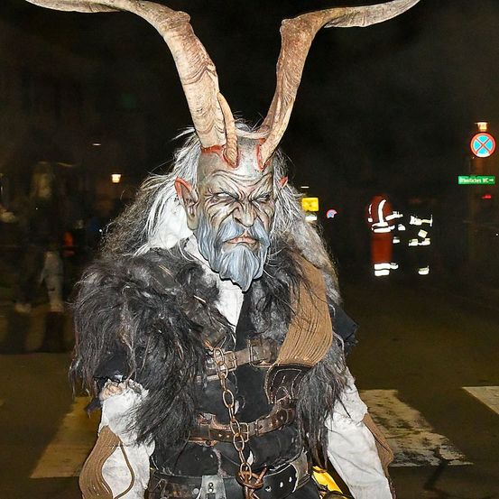 Eine Person in einem Wikingerkostüm mit langen Hörnern auf dem Kopf steht nachts auf der Straße.