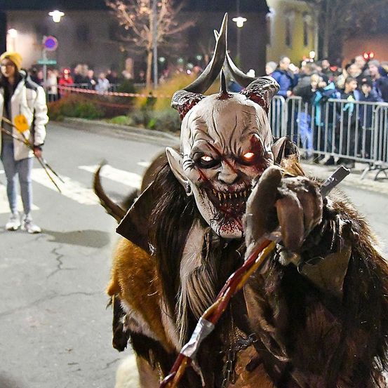 Eine Person in einer Dämonenmaske geht nachts auf der Straße, während eine Menge zuschaut.