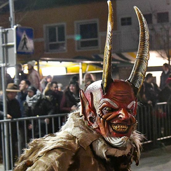 Eine Person mit einer roten Maske mit Hörnern und einem gruseligen Gesicht steht bei Nacht vor einer Menschenmenge.