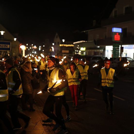 Eine Gruppe von Menschen in Warnwesten mit brennenden Fackeln geht bei Nacht die Straße entlang.