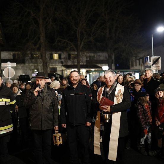 In der Nacht spricht ein Mann mit einem Mikrofon zu einer Menschenmenge. Neben ihm steht ein Mann mit einer Laterne. Ein anderer Mann mit einem Buch und Kelch steht rechts.