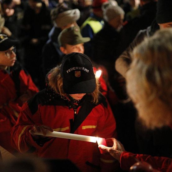 Eine Gruppe von Feuerwehrleuten und Freiwilligen hält brennende Kerzen bei einer Gedenkfeier bei Nacht.