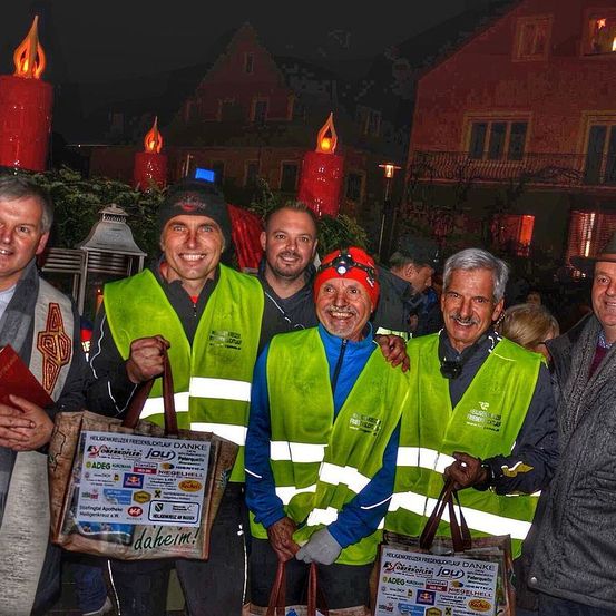 Eine Gruppe von Männern in reflektierenden Westen lächelt für ein Foto vor einem Gebäude mit brennenden Kerzen bei Nacht.