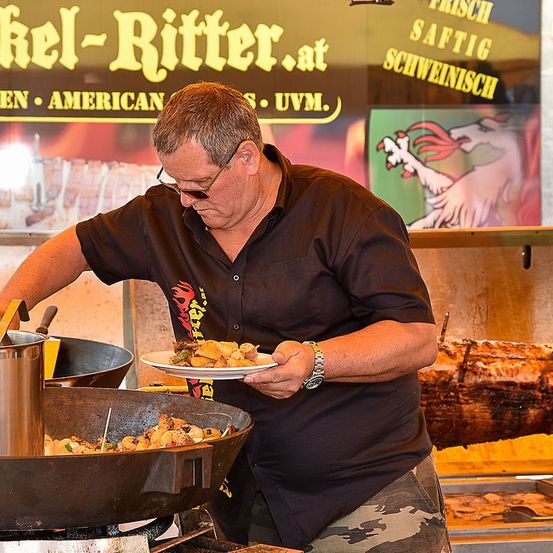 Ein Mann mit Brille und schwarzem Hemd kocht in einer großen Metallpfanne in einem Restaurant.
