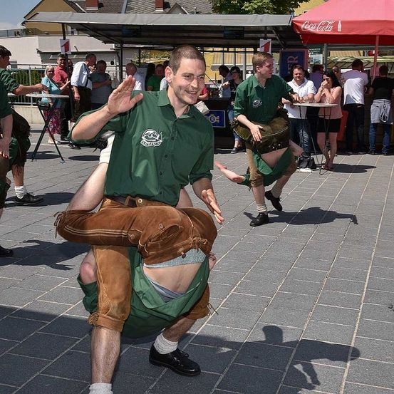 Ein Mann in einem grünen Hemd und braunen Hosen tanzt und trägt einen Mann auf seinem Rücken in einem Außenbereich.