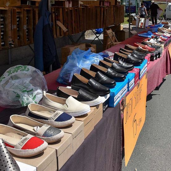 Ein Schuhverkaufsdisplay mit verschiedenen Paaren von Schuhen auf Kisten, einige mit Preisschildern, auf einem roten Tisch, der mit einem schwarzen Tuch bedeckt ist.