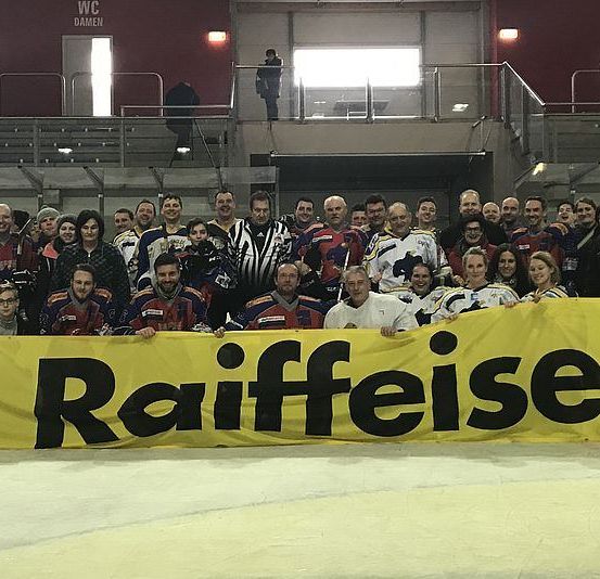 Eine Gruppe von Menschen steht zusammen und hält ein gelbes Banner, das Raiffeisen steht. Sie sind auf einer Eisbahn.